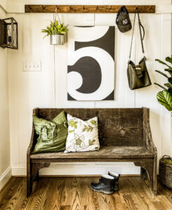 Straight on view of foyer bench, green and leafy pillows with a peg rack above.