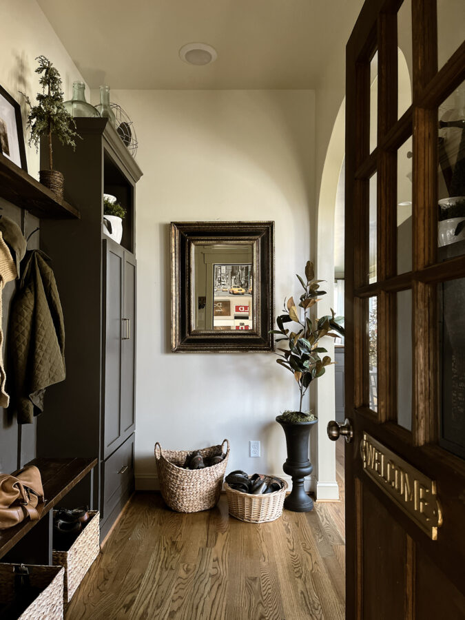 Mudroom entry with a chunky framed mirror and basket to hold shoes, built in cabinets painted in urbane bronze